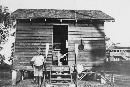 Photograph of a fisherman standing outside at shack at Bribie Island, c.1925.