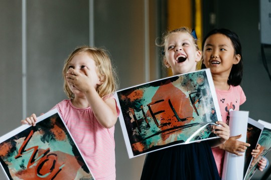 Three children holding up posters with words on them