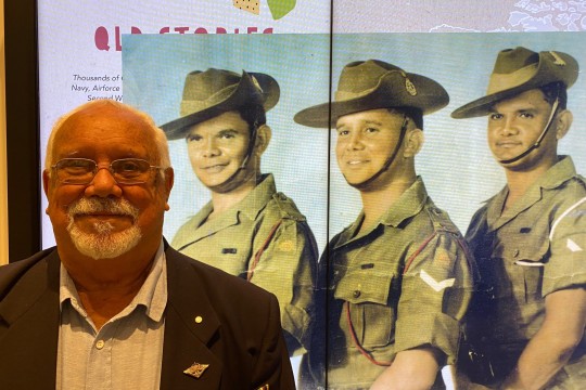 George Bostock standing in front of a enlarged photo of himself as a young soldier