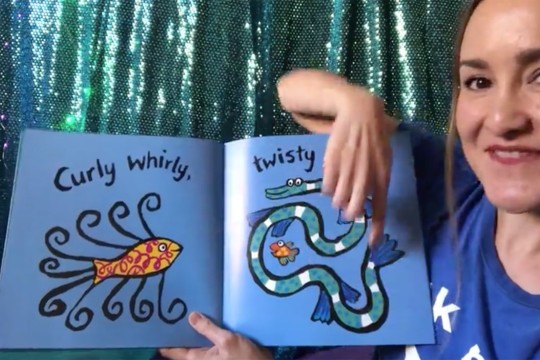 Picture book with fish read by girl in blue tshirt