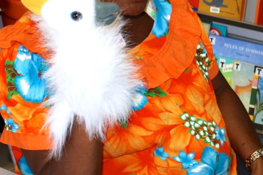 A woman in a colourful shirt plays with a cockatoo puppet in an Indigenous Knowledge Centre. The child she is playing with is out of frame.  