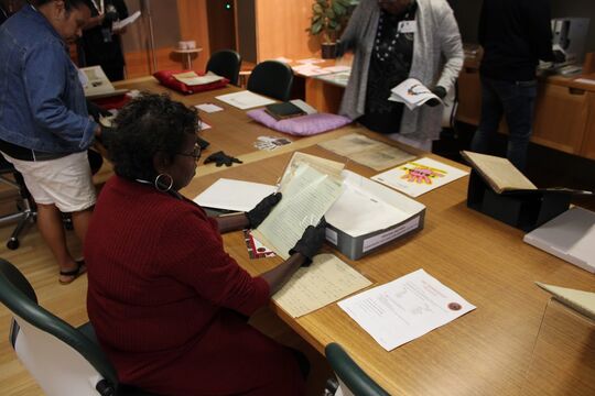 A group of First Nations people at a Black Gloves experience, interacting with collection materials.