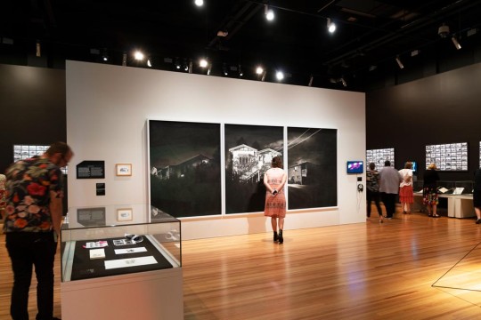 Woman observing Ian Strange's charcoal artwork in the Home exhibition.