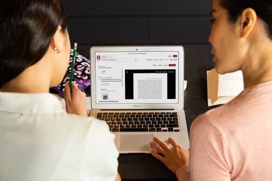 Over the shoulder photo of two people using the JSTOR website on a laptop.