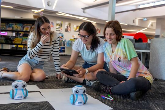 3 teenager sitting on floor in library with tablet