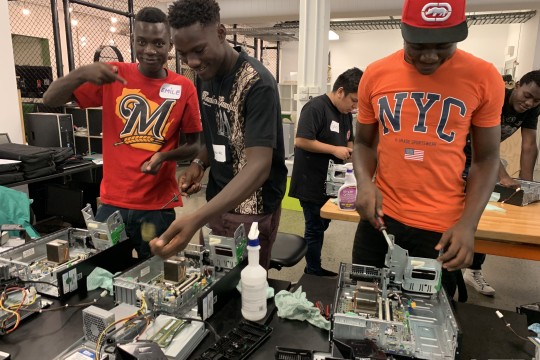 Three young men smiling and working on the inside of computer cpus