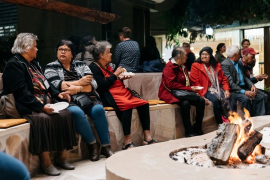 Visitors chatting and eating while gathered around a lit fire in the Talking Circle. 