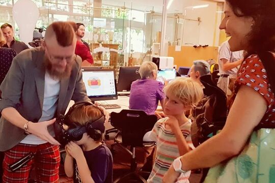 Man helping child with VR headset while lady and other child look on