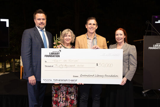 Four people smiling and holding a large presentation cheque