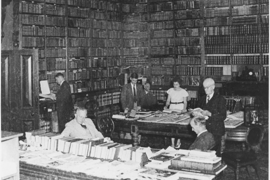 Black  white photograph of seven individuals working in a library