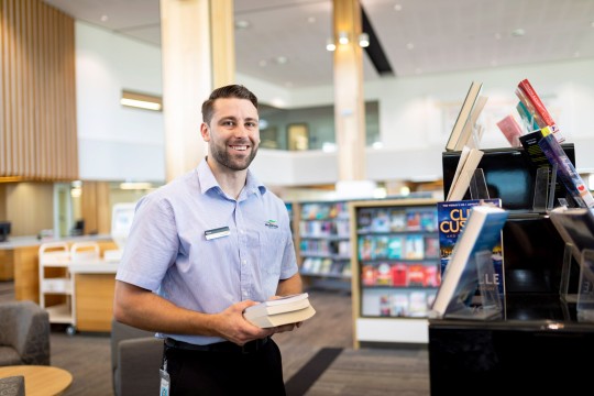 Librarian in uniform holding books and smiling at the camera 