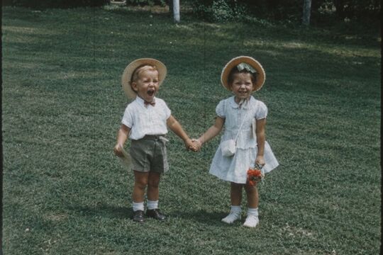 Two small children holding hands in a backyard.