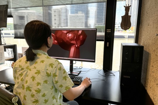 A photo of a person sitting at a computer monitor with a 3d model on the screen