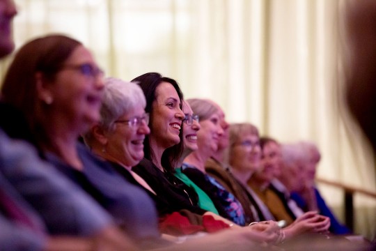 Row of people seated in an auditorium smiling and clapping.
