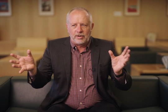 Man in a suit sitting and gesturing with hands. 