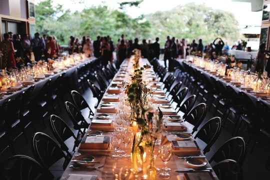 Long tables set with dinnerware, chairs, and flowers for a wedding on the Queensland Terrace, with a crowd of guests in the background.