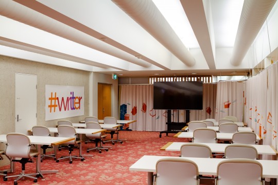 A long view of the Queensland Writers Centre (QWC) workshop room showing tables, chairs and a large TV