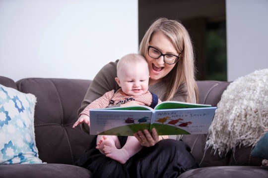 Woman sitting at home reading a book with her baby