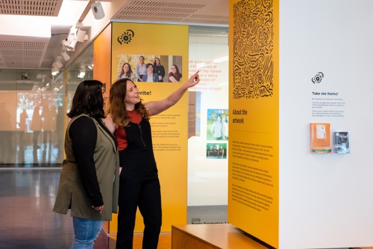 Two visitors looking and pointing at artwork in State Library's showcase Sovereign Stories.