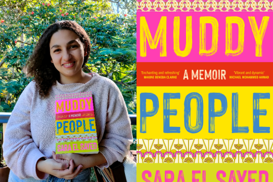 Sara El Sayed wears a jumper and jeans she stands outside in front of a tree and holds her book Muddy People