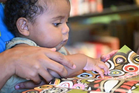 Baby looking through the book My People 2022 photography by Saltwater People State Library of Queensland