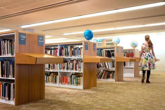 A woman is walking past a row of book shelves with globes on top of them