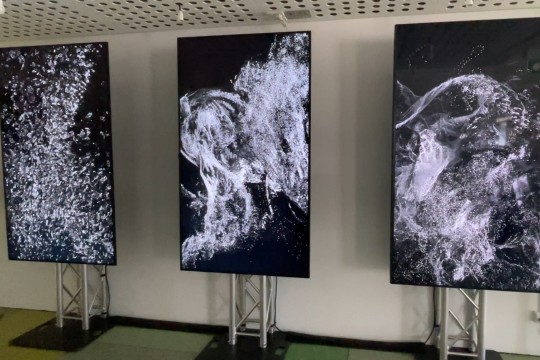 A photo of three vertical screens with black and white point cloud artwork