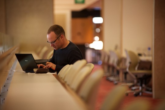 Man using a laptop near the information collections at State Library.