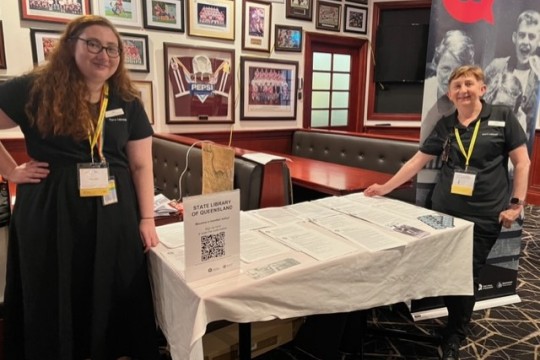 Two State Library staff members standing by the exhibitor stall for State Library at the Sands of Time Conference 2022
