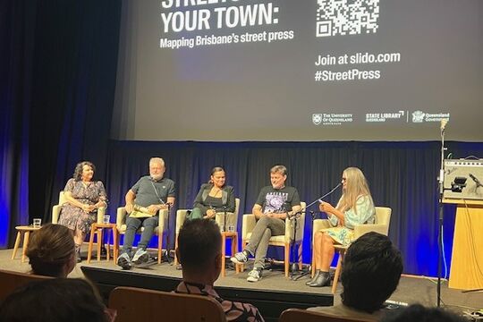 A panel of 5 speakers sits onstage in an auditorium. Above them the screen says Streets of your town: Mapping Brisbane's street press.