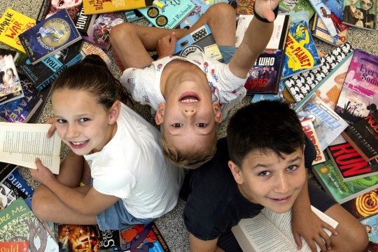 A girl and two boys surrounded by a pile of books