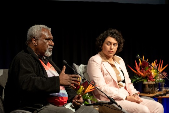 Man and woman talking into microphones on a stage.