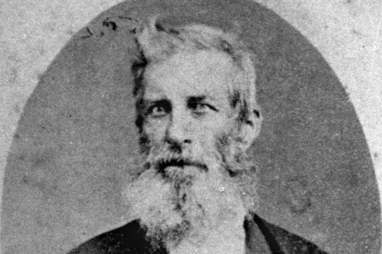 Portrait of Thomas Dowse, a caucasian man with a large whispy beard and cropped hair with a cowlick at the front. He is wearing an 1800's suit.