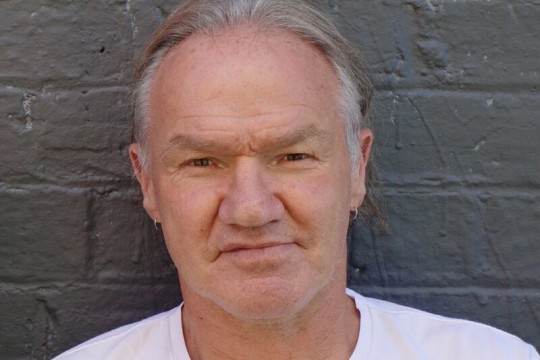 A picture of a man in a white shirt with a brick wall in the background