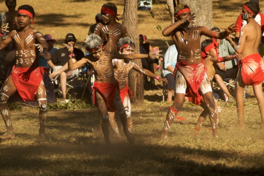 Boys performing an aboriginal dance on dry grass 