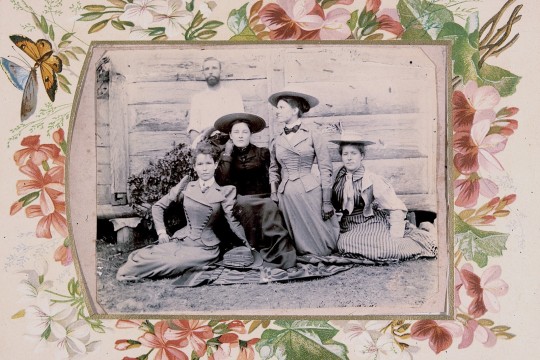 A group of four women and one man sitting outside a wooden house
