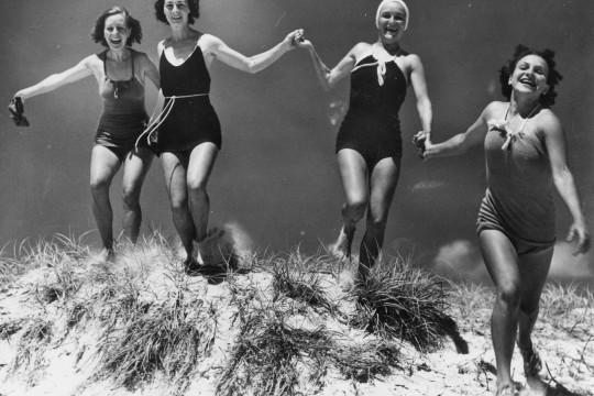 Four women running down a sand dune in swimwear