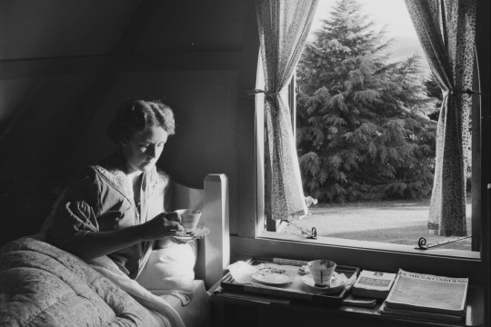 Woman lying in bed with a cup of tea at the High Tor guesthouse