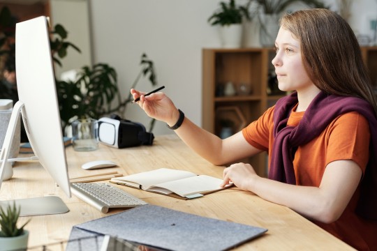 Young teenager writing in front of a computer screen