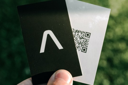 A hand holding two black and white business cards in front of a green background