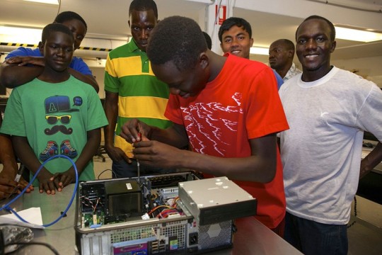 Participant in a CCC workshop fixing a computer surrounded by spectating classmates