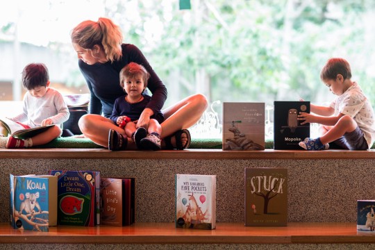 3 children with 1 adult lady in the corner looking at books