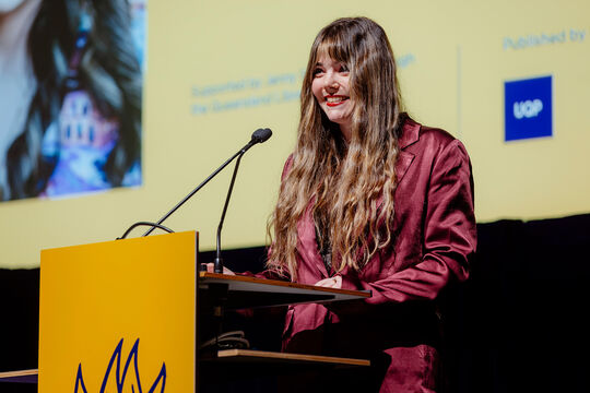 Emily Lighezzolo behind a lecturne on stage at the QMA