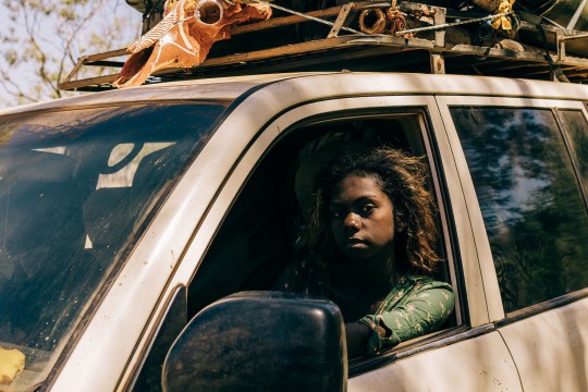 Two people in a car with items stored on the foor.