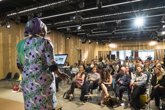 A young woman presents a talk to a group of onlookers.