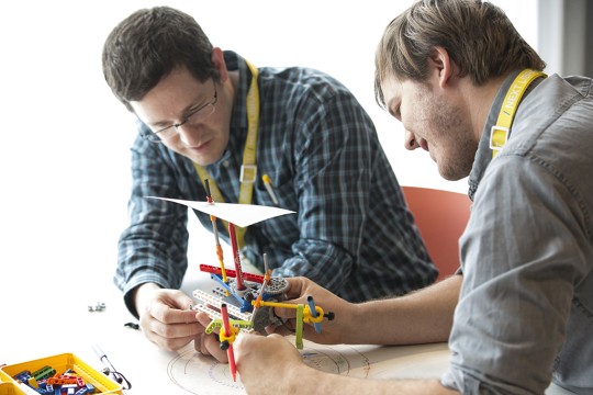 Two men work on a design project with sticks and rubber bands.