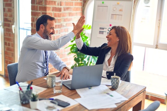 Man and woman sitting at a desk hi-fiving each other