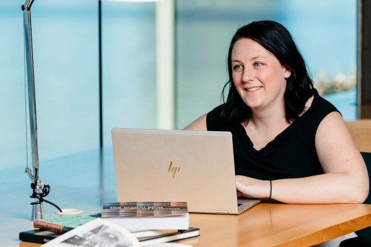 Woman using laptop sitting at a desk in the State Library of Queensland overlooking the rive