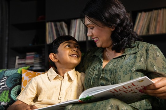 Child smiling at mother who is reading him a story