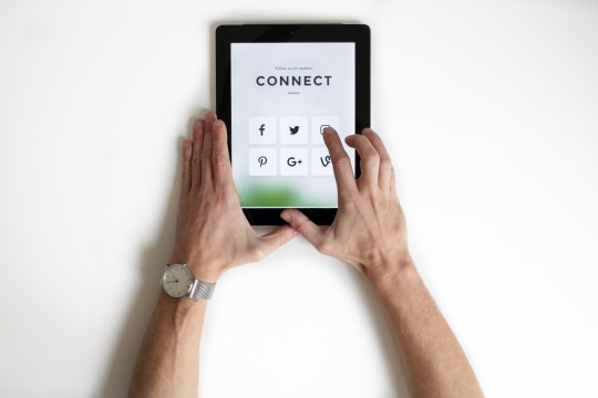 Two hands holding an ipad displaying social media icons